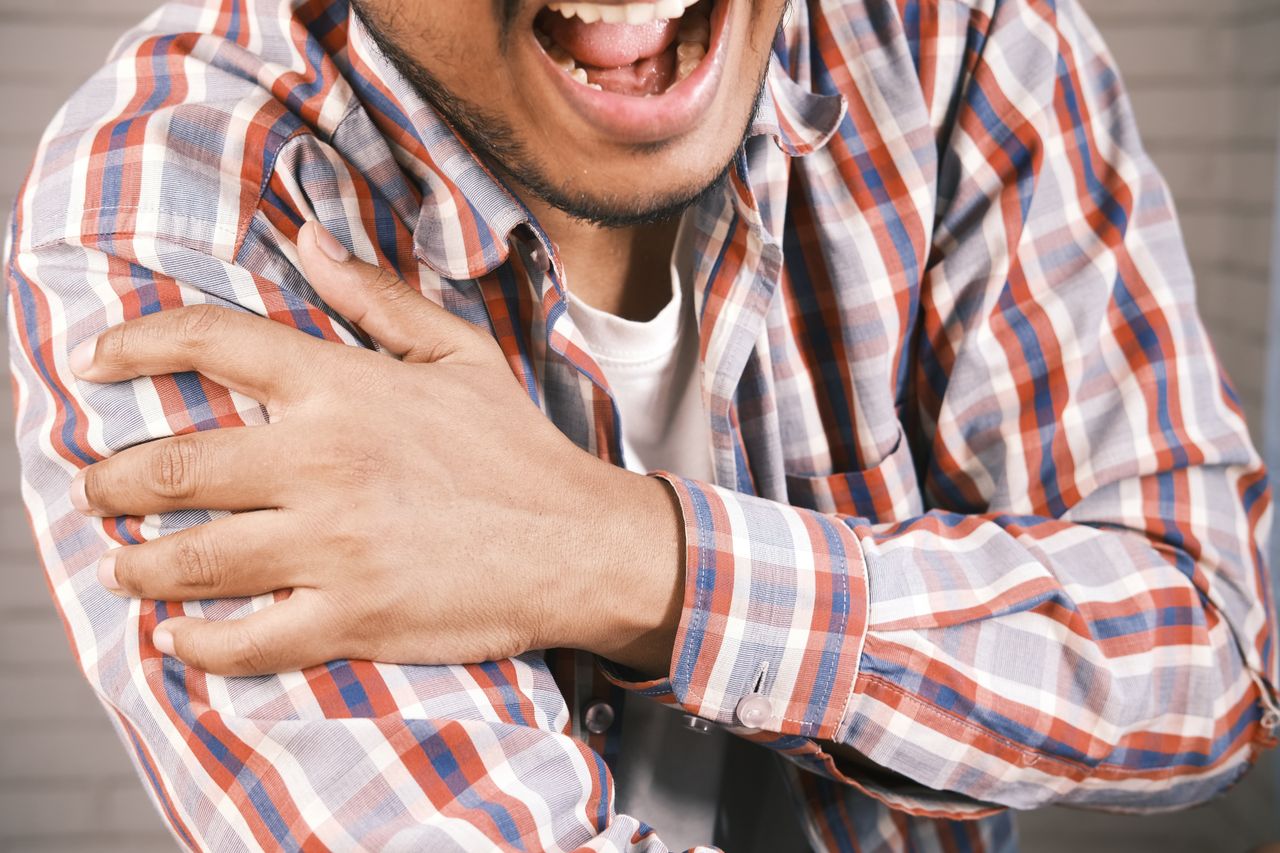 services-02 Close-up of a man in plaid shirt experiencing shoulder pain, grasping his arm.